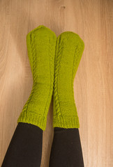 A woman wearing warm hand craft socks. Knitted from a natural sheep wool yarn. Winter clothing. On a wooden background.