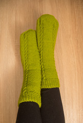 A woman wearing warm hand craft socks. Knitted from a natural sheep wool yarn. Winter clothing. On a wooden background.