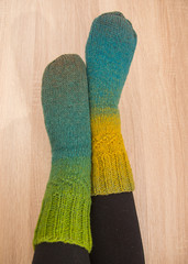 A woman wearing warm hand craft socks. Knitted from a natural sheep wool yarn. Winter clothing. On a wooden background.