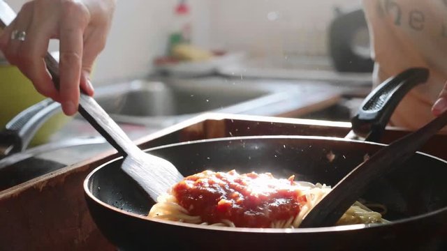 Cooking and stirring the spaghetti with red tomato sauce in the frying pan.