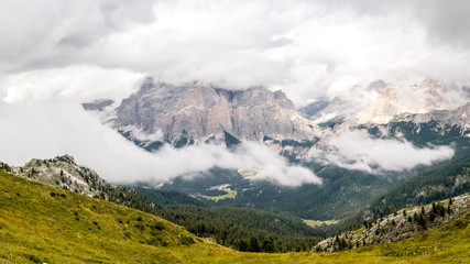 High rocky peaks and a wooded valley in fog and white clouds in Dolomites, South Tyrol, Italy