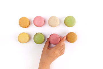 Girl's hand taking pink French macaron from two rows of colorful macarons isolated on white