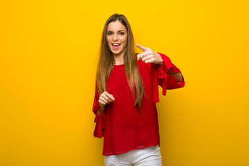 Young girl with red dress over yellow wall frustrated by a bad situation and pointing to the front