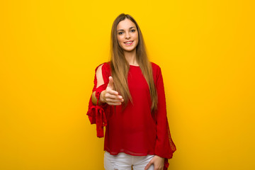 Young girl with red dress over yellow wall shaking hands for closing a good deal