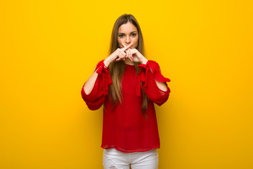 Young girl with red dress over yellow wall showing a sign of silence gesture