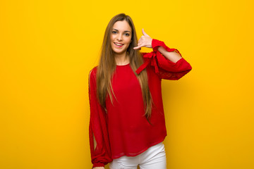 Young girl with red dress over yellow wall making phone gesture. Call me back sign