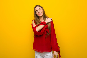 Young girl with red dress over yellow wall suffering from pain in shoulder for having made an effort