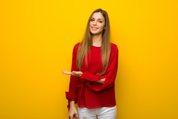 Young girl with red dress over yellow wall presenting an idea while looking smiling towards