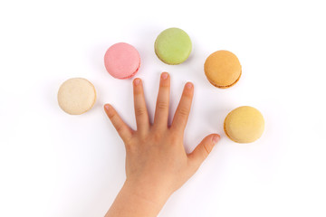 Child's hand spreading fingers with five colorful macarons on white background