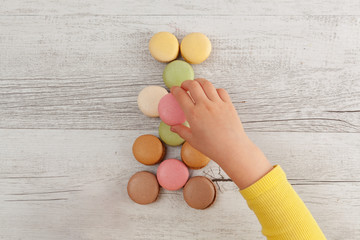 Child arranging macarons on white rustic wooden table - top view with copy space
