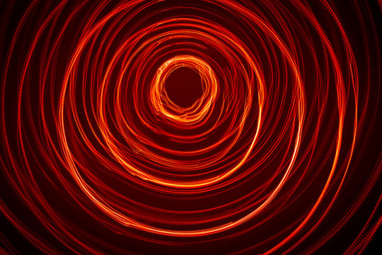 A beautiful, bright light swirl of red color. Futuristic light painting on a black background. Round light circles