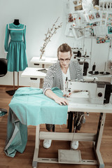 Long-haired fashion dressmaker in a striped jacket doing tailoring