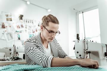 Long-haired young fashion dressmaker in eyeglasses working in a showroom