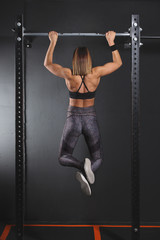Woman athlete executing pull up in gym