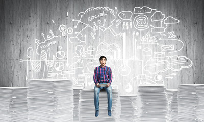 Attractive man sitting on pile of paper documents.