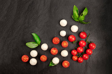 A flat lay composition with Mozzarella cheese, cherry tomatoes and basil on a black background, Italian cuisine ingredients with copy space