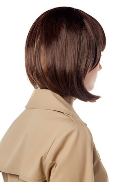 A close up back view side shot of a lady with dark brown short haircut,  wearing a beige trench coat with a collar. The girl is posing on white  background. New-fashioned hairstyle.