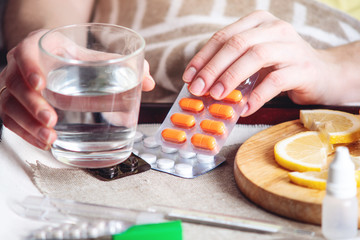 Thermometer pills water and lemon on tray. Person with a cold is treated in bed. Colds, flu and treatment