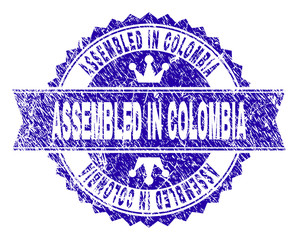 ASSEMBLED IN COLOMBIA rosette seal imprint with distress style. Designed with round rosette, ribbon and small crowns. Blue vector rubber print of ASSEMBLED IN COLOMBIA tag with corroded style.