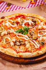 Italian Pizza with seafood and mozzarella cheese on wooden cutting board. Close up