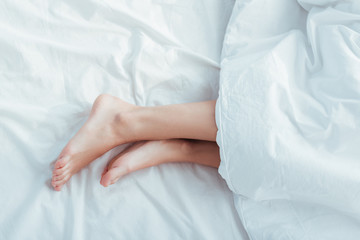 low section of female legs under blanket in bed