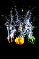 Fresh colourful bell pepper splashing in water on black background.