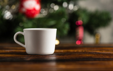 Cup of coffee or tea on a wooden table against the background of a Christmas tree