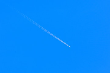 Airplane contrail in clear blue sky with plane trails.