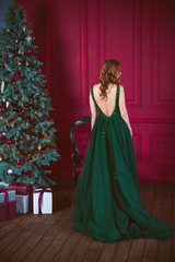 Winter holidays, celebration and people concept - young sexy woman in elegant green evening dress over christmas interior background