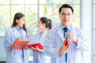 A handsome professor checking liquid in beaker for young beautiful asian woman scientist watching substance in chemistry experiment in hospital lab. Portrait of science & healthcare concept.