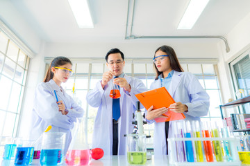 A handsome professor checking liquid in beaker for young beautiful asian woman scientist watching substance in chemistry experiment in hospital lab. Portrait of science & healthcare concept.