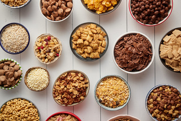 Assortment of different kinds cereals placed in ceramic bowls with cornflakes, granola, cereals and oatmeal. The concept of breakfast food. Flat lay, top view on white wooden table.