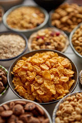 Obraz na płótnie Canvas Close up and selective focus. Composition of different kinds cereals placed in ceramic bowls with cornflakes, granola, cereals and oatmeal. Flat lay, top view on white wooden table.