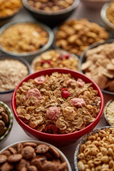 Close up and selective focus. Composition of different kinds cereals placed in ceramic bowls with cornflakes, granola, cereals and oatmeal. Flat lay, top view on white wooden table.