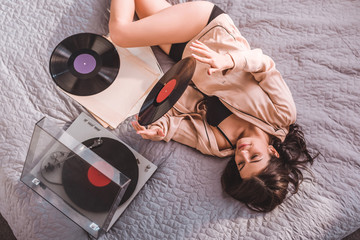 high angle view of woman laying on bed and listening vinyl audio player at home