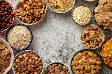 Assortment of various kinds cereals placed in ceramic bowls with cornflakes, granola, cereals and oatmeal. Flat lay, top view on white rusty table with copy space in the middle