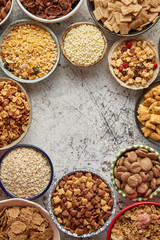 Assortment of various kinds cereals placed in ceramic bowls with cornflakes, granola, cereals and oatmeal. Flat lay, top view on white rusty table with copy space in the middle