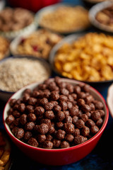 Assortment of various kinds cereals placed in ceramic bowls with cornflakes, granola, cereals and oatmeal. Flat lay, top view on blue rusty table with copy space in the middle. Selective focus.