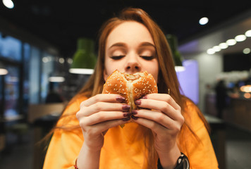 Close photo of a beautiful girl and a burger.Girl closes her eyes and smells the scent of a...