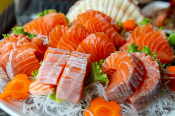 A full size for traditional Japanese food name “Sashimi” included orange with white strip belly and meet served on white big bowl on ice, decorated with carrot flower shaped. Side view shot.