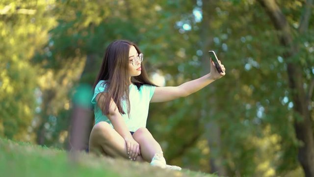 The girl is taking pictures of herself on the phone. Beautiful teen girl doing selfie. The girl makes selfie.