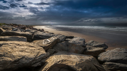 Big rocks in front of the sandy beach at Waterville, County Kerry, Ireland, glaring under the...