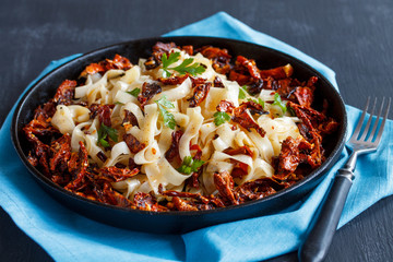 Pasta with sun-dried tomatoes and parsley on a cast iron pan on a blue napkin, on a gray background.