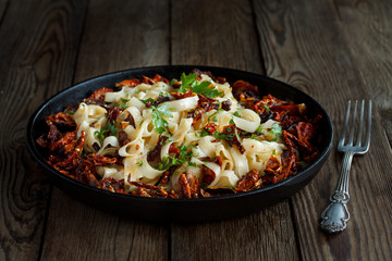 Sun-dried tomatoes with pasta, parsley in iron black pan and fork, on natural wooden background.