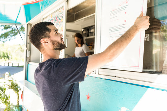 Confident young male salesman positioning menu placard on food truck