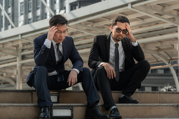 Asian business man sitting on a staircase between a tall building, stressed and fear by a business...