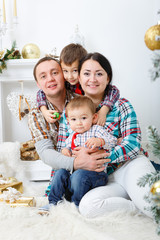Parents and two little children having fun and playing together near Christmas tree indoors. Happy family concept