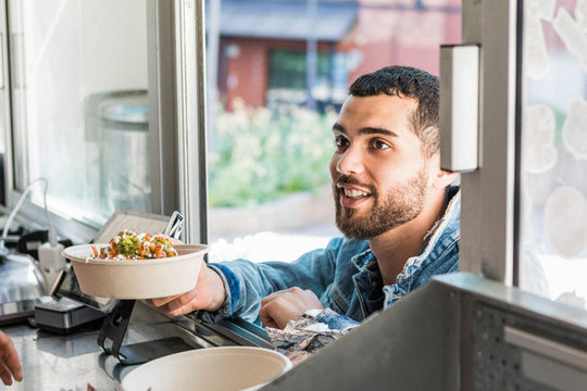 Smiling young male customer holding fresh Tex-Mex in bowl at concession stand