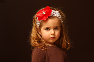 Portrait of cute two year old toddler with a red flower headband, isolated on black