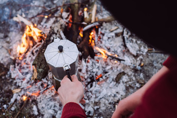 Winter vacation. Tourist  in  hat  cook coffee on campfire in winter time. Concept adventure active vacations outdoor. 